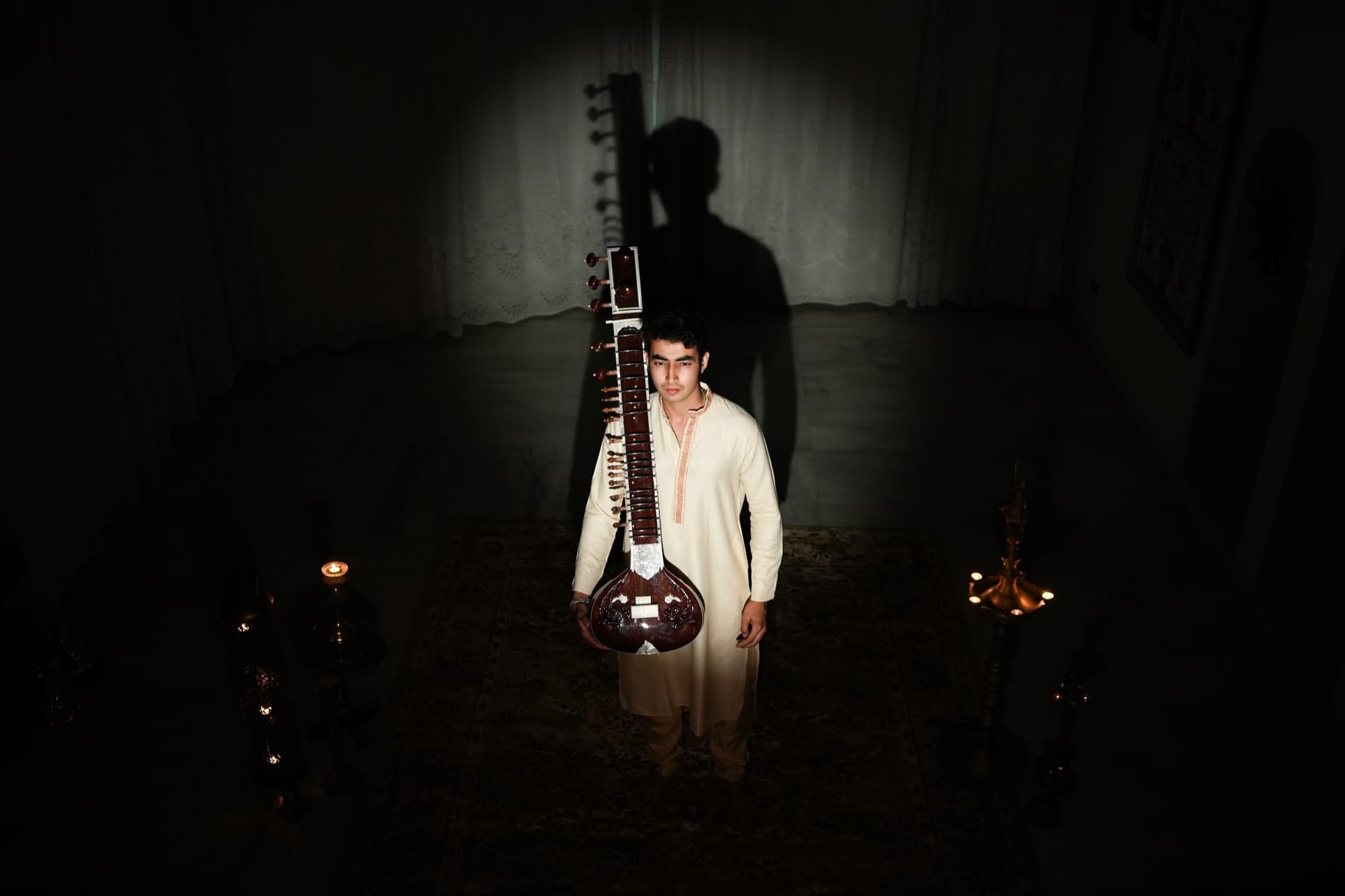 Pradhyuman standing with his sitar in a single dramatic light